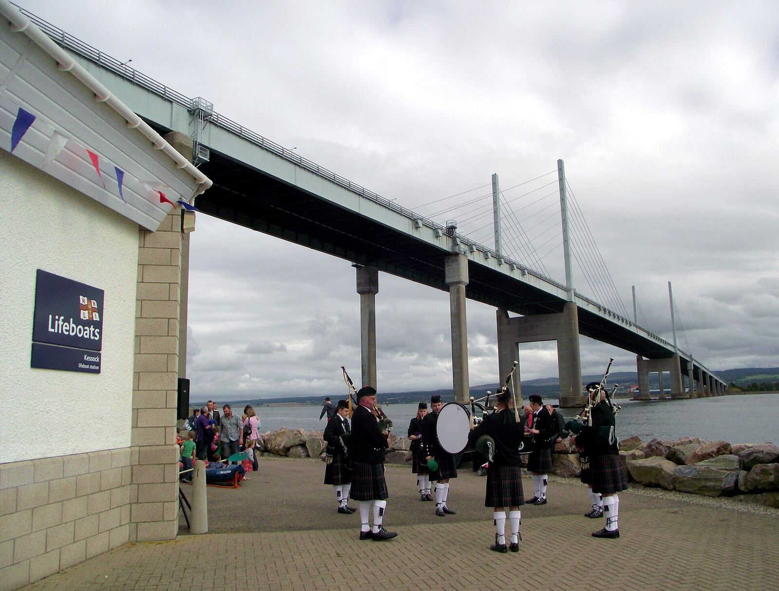 What a backdrop - the magificent Kessock Bridge. The village of Kessock (a.k.a. North Kessock) lies directly across the Beauly Firth from the City of Inverness. Until fairly recently, a ferry ran between the two, but since 1982 the imposing Kessock Bridge (carrying the A9 trunk road north from Inverness) has joined the two communities. en.wikipedia.org/wiki/Kessock_Bridge Kessock lies directly opposite the mouth of the River Ness, and Inverness Harbour and Marina, and the entrance to the Caledonian Canal is close by too. As a busy arm of the North Sea/Moray firth., the Beauly Firth is an important maritime route, both for commercial and leisure traffic. It took a long time to get a lifeboat based in the Inverness area but now that we do have the facility, locals are extremely proud - and supportive - of the Kessock lifeboat and its brave crew. The Lifeboat station is located at Craigton Point, directly under the north end of the Kessock Bridge. Several Band members have family or friends in the crew, hence we were delighted to be able to support and assist at the RNLI Kessock Station open day today (24th August 2013) by providing a mini-band to entertain the visitors. Kessock is one of Scotland’s youngest lifeboat stations, operating an inshore B class Atlantic 75 lifeboat – “The Moray Dolphin”. For over 10 years the lifeboat crews have launched the lifeboats, not only to save lives at sea but also to save lives inland during flooding. rnli.org/findmynearest/station/Pages/Kessock-Lifeboat-Sta...